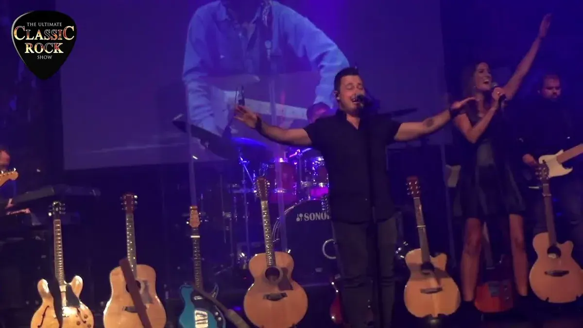 The Ultimate Classic Rock Show singer with arms raised, guitars racked behind