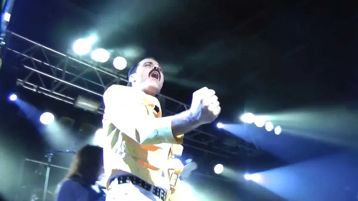 Almost Queen frontman Joseph Russo as Freddie Mercury in a yellow jacket on stage